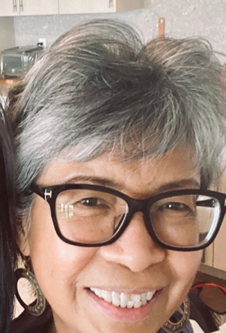 Nora, a Filipino woman, with short gray hair, black framed glasses, smiling.