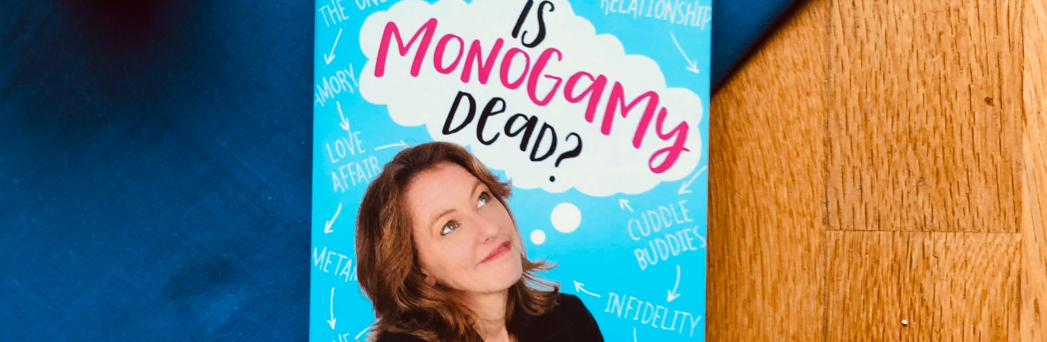 A paperback copy of “Is Monogamy Dead” by Rosie Wilby placed on a wooden table next to a mug of black coffee on a blue tablecloth. The cover has a photo of the author, a white, middle aged woman, looking up at the title.