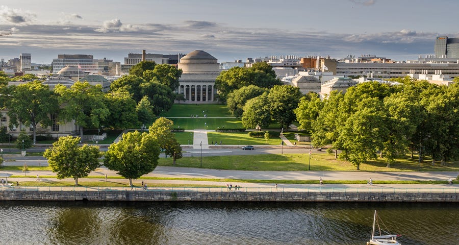 Aerial photo of MIT’s Great Dome with a lawn, trees, and a river in the foreground.