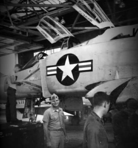 Military man smiling standing in front of fighter jet.