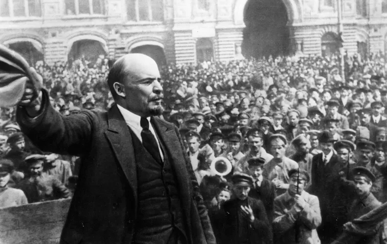 A black and white photo from 1917. A man with a goatee wearing a suit holds out his hat and gives a speech to a large crowd.