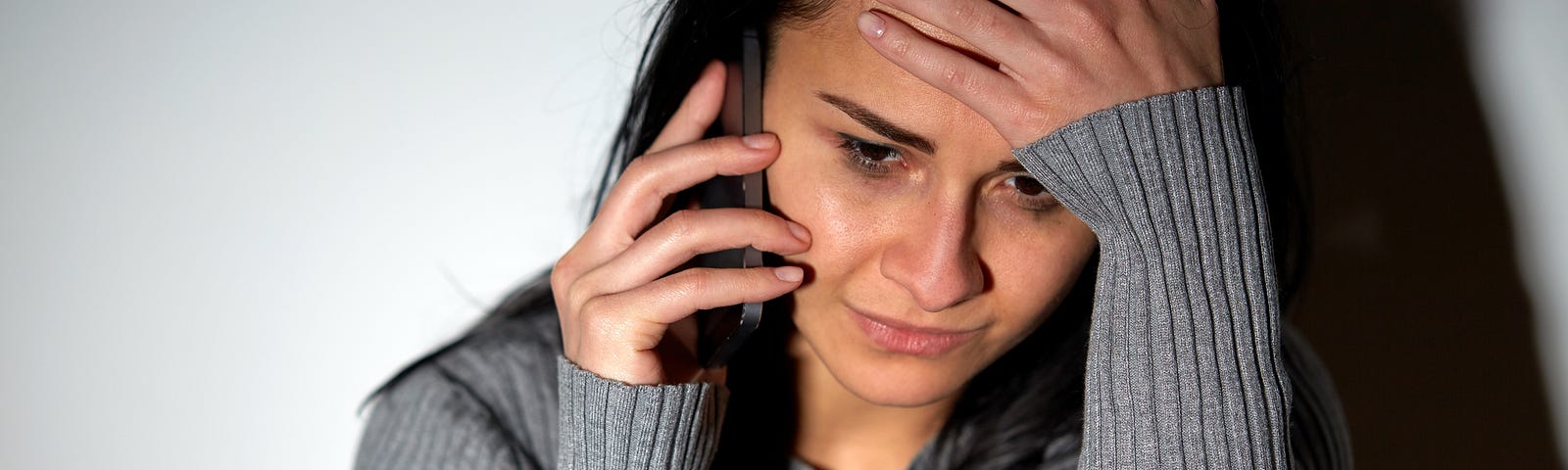 A woman wearing a gray sweater crying while on the phone (telephone psychic, self-disclosure, child abuse, rape)
