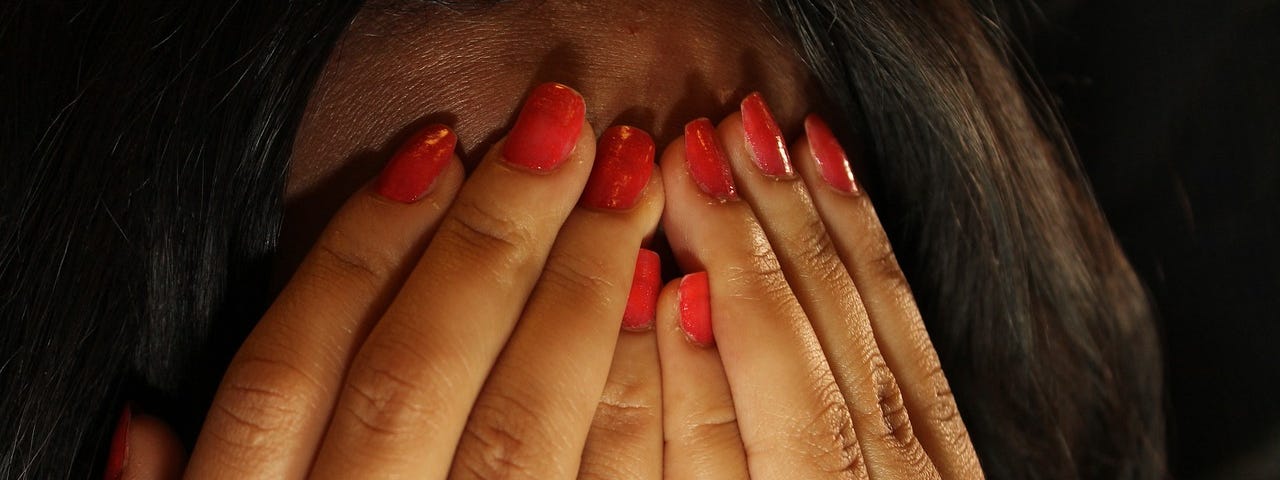 Image of a person holding their hands over their face, their nails painted red.