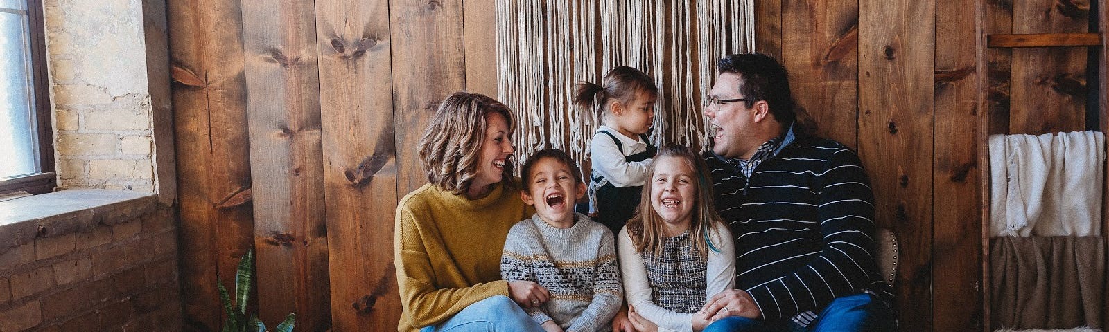 The Shoup family (parents w 3 kids) sitting on a bench, smiling and laughing.