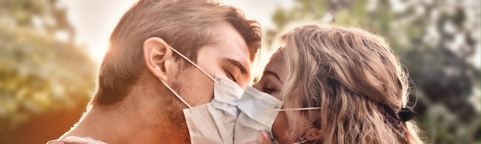 A couple (in masks) embrace for a kiss in the afternoon light.