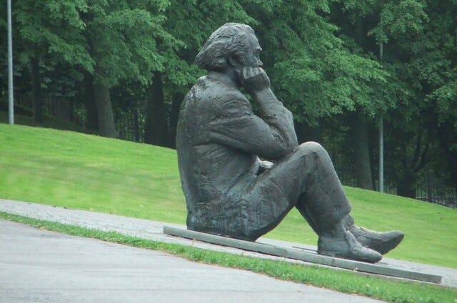 A statue of a man in 19th century clothes sitting on the grass thinking.