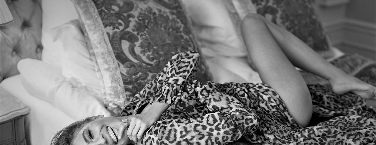 Woman laying on the bed in a leopard print dress with bare feet.