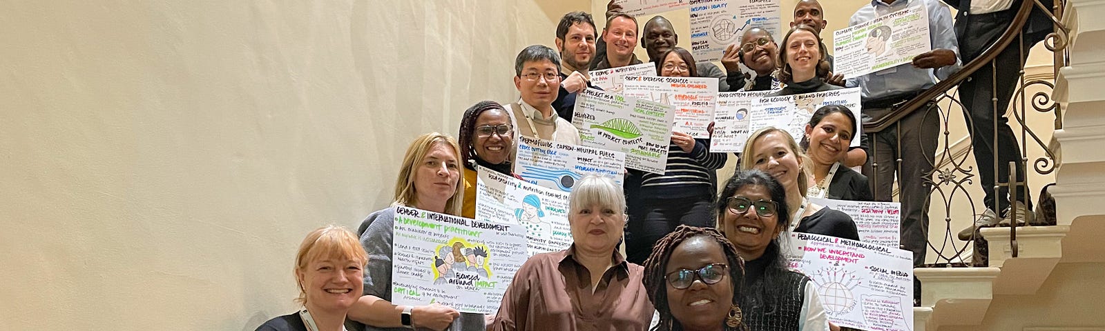 Global crucible participants stand on a staircase holding the posters depicting their research areas