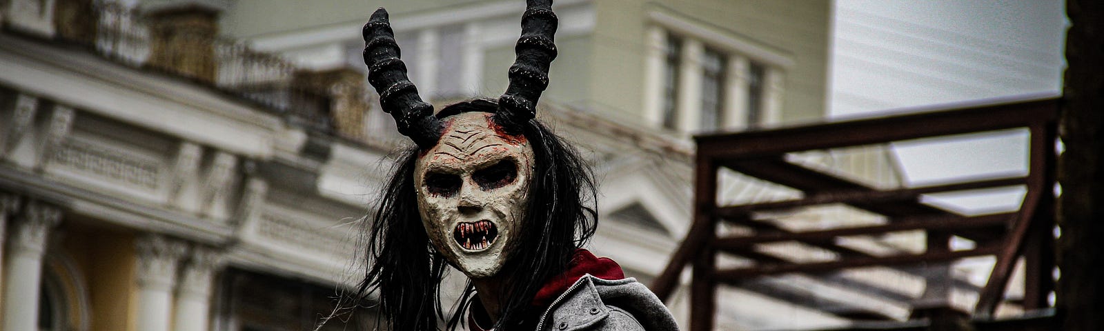 A man outdoors wearing a fright mask with horns.