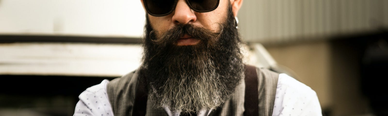 A tough guy with a big beard, sunglasses, a vest, a shirt and tie, and tattoos.