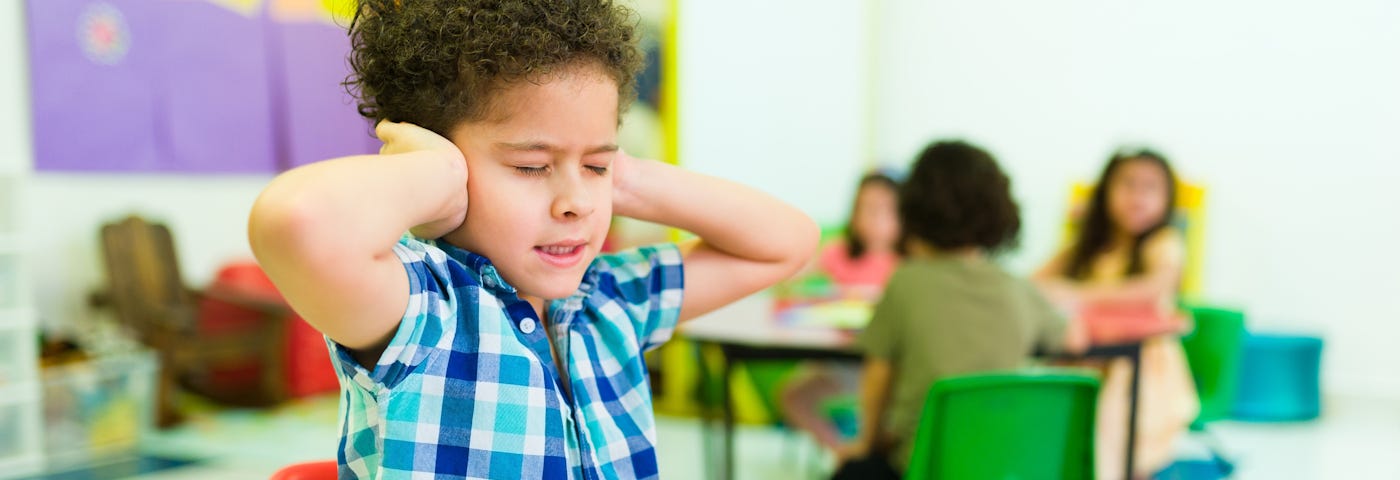 Autistic boy covers ears to block loud noise in preschool setting.