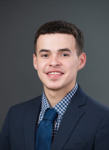 Alex Garcia is pictured in a navy blazer against a dark gray background