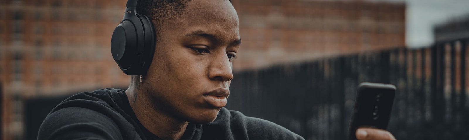 Man wearing headphones looks at a cellphone.