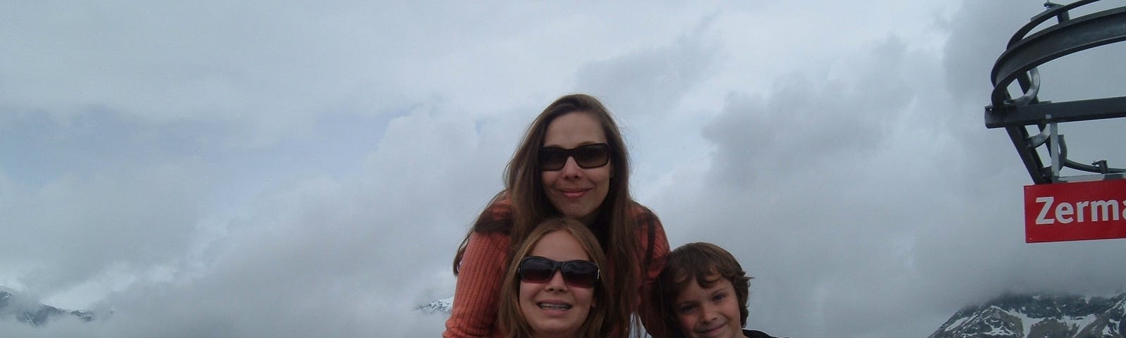 The author with her two children on a mountain in Zermatt. Her daughter is sitting in a wheelchair and her son is leaning against his mom and sister.