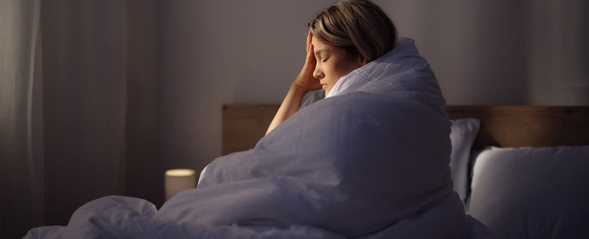A woman is proped up in bed with her hand shielding half her face.