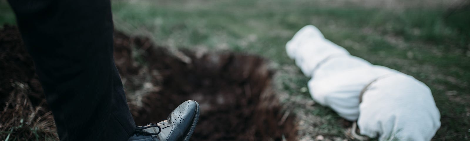 A man in dress shoes and slacks buries a wrapped body in the wilderness.