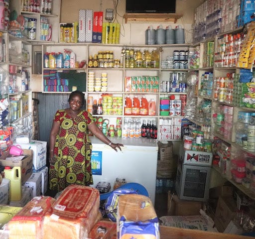 A woman stands next to a refrigerator/freezer inside a shop with lots of products neatly shelved.