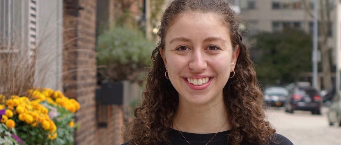 A headshot of Jennifer Bindman in a black long sleeve t-shirt in front of a New York City street.