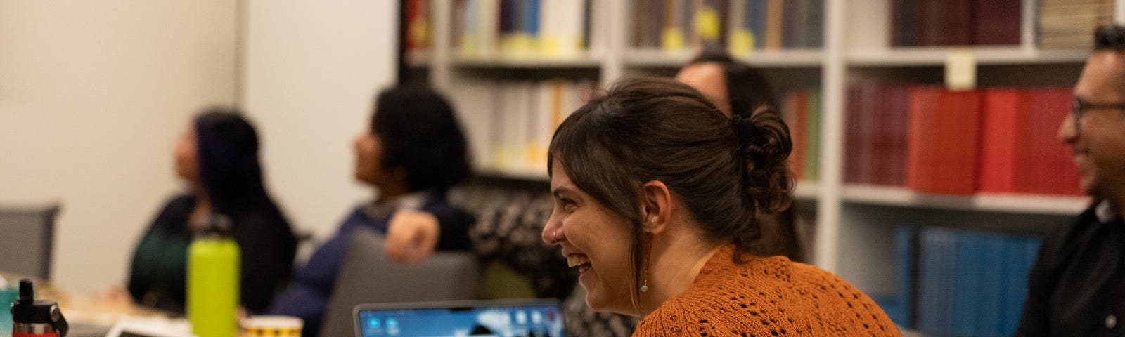 A woman sits at a table engaging in conversation with other scholars.