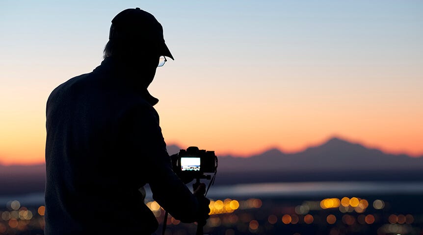 The silhouette of a man photographing a sunset cityscape