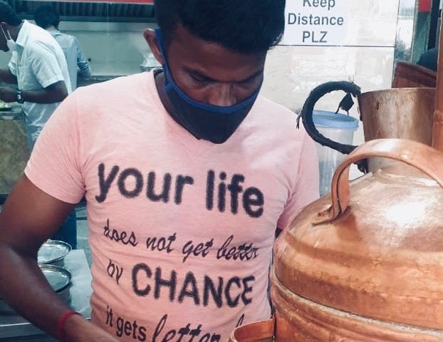 A chaiwalla in India making tea with a funny T-shirt.