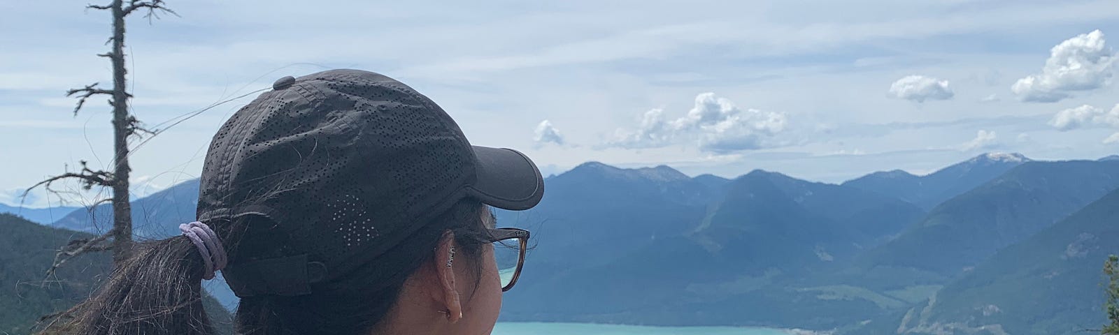 A woman gazes at mountains and a crystal blue lake in the distance.
