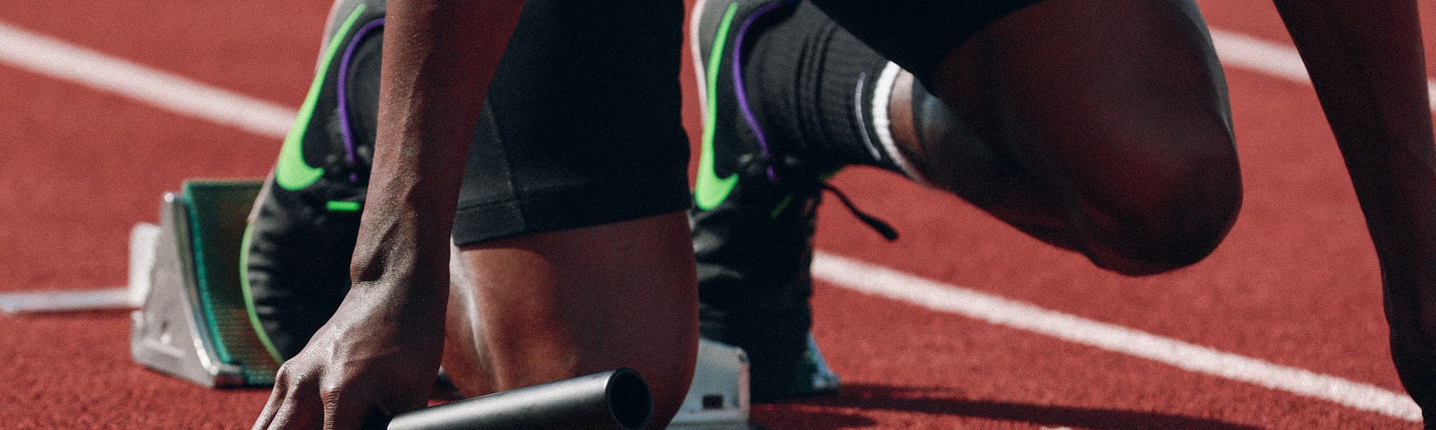 a closeup of a runner crouched at the starting blocks at a track