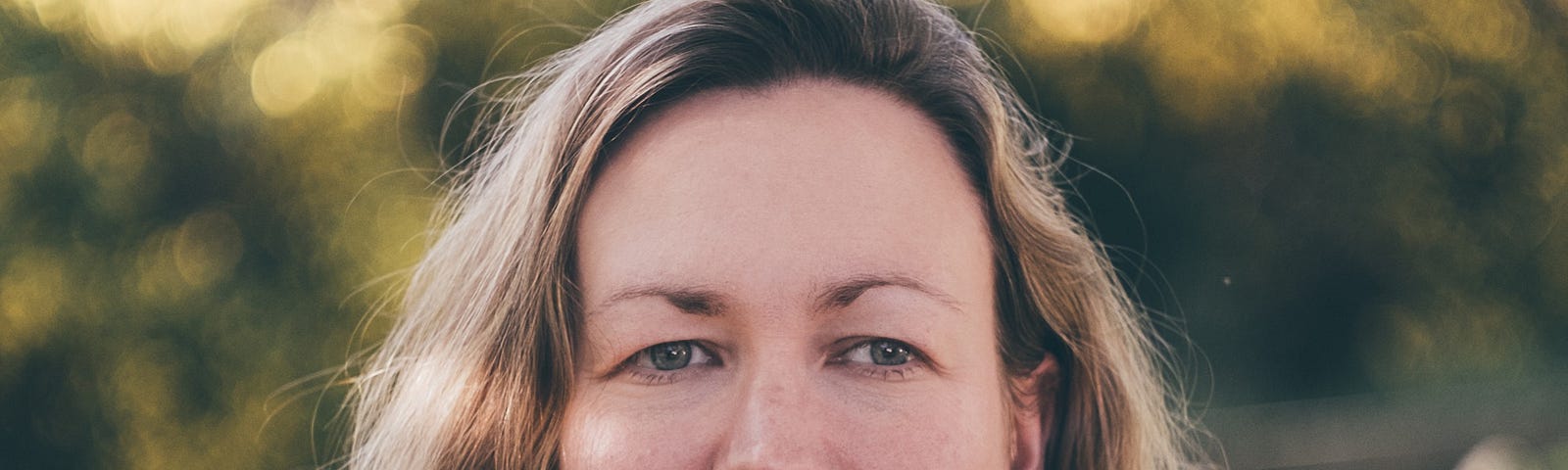 Headshot of the writer Helen Sedgwick. She is standing in a garden with blurred green and golden trees behind her.