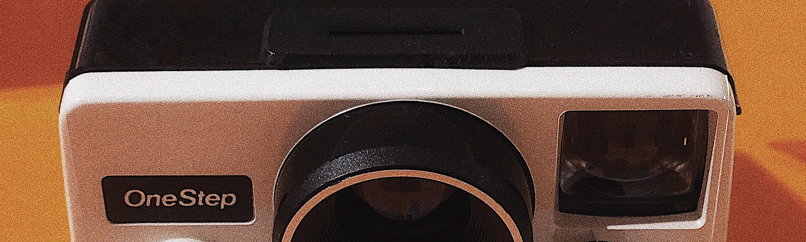 White Polaroid Land Camera with a One Step red button and rainbow running down the middle. This image has an orange background.