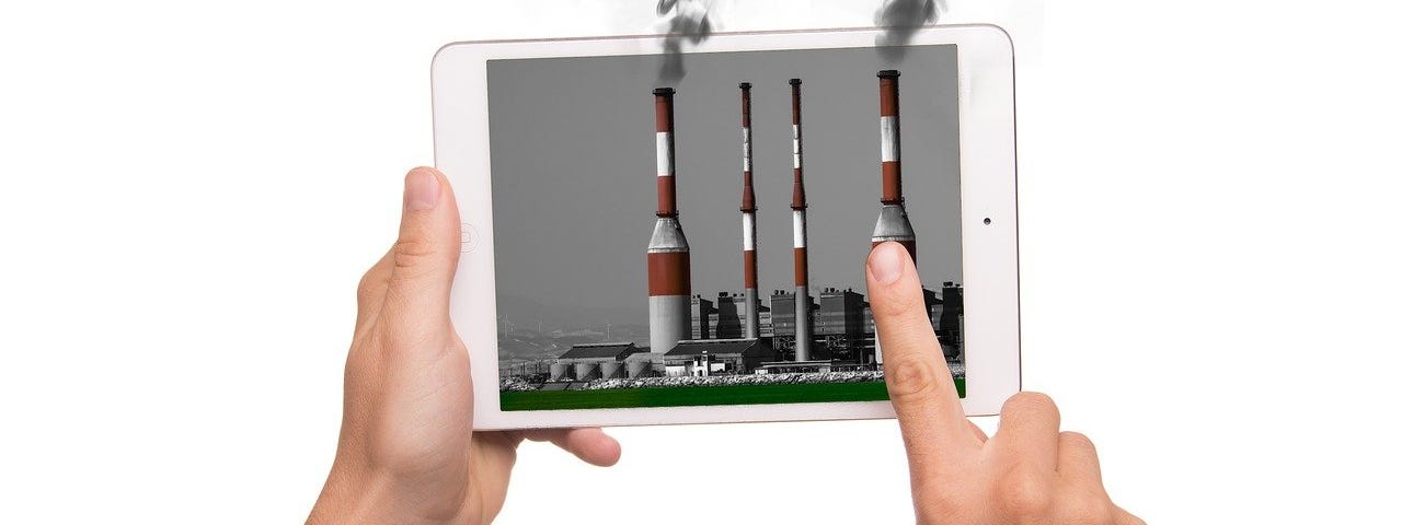 IMAGE: Two hands holding an iPad with four industrial chimneys emitting black fumes.
