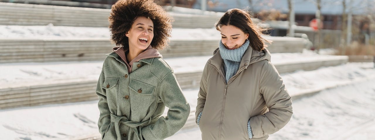 Two smiling women walk together through the snow