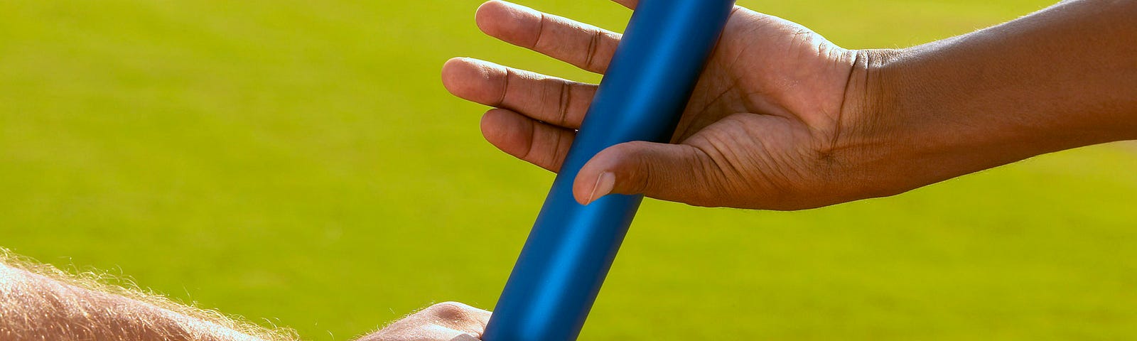 A close up of two runners’ hands as they pass a blue baton during a relay race.