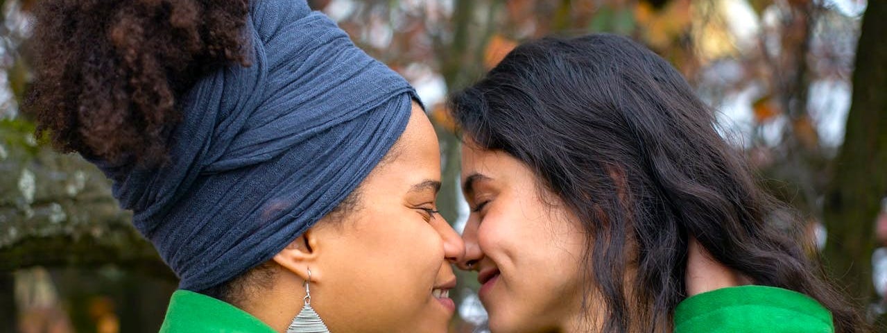 close up of two female presenting people nose-to-nose smiling as if they are about to kiss or just did