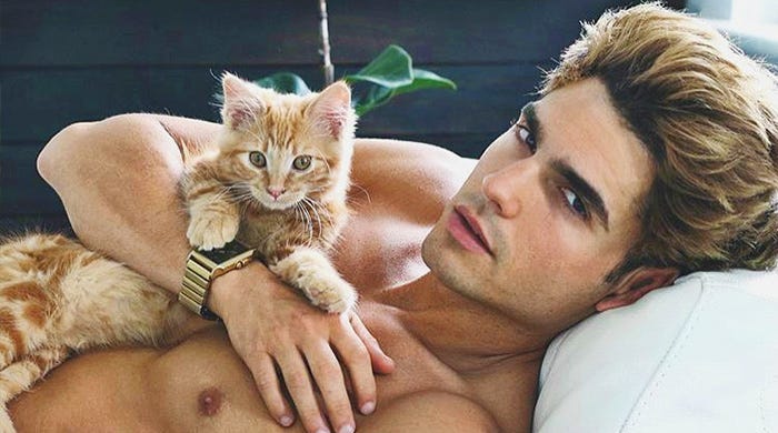 Photo of blond haired man lying down with a yellow kitten on his chest.