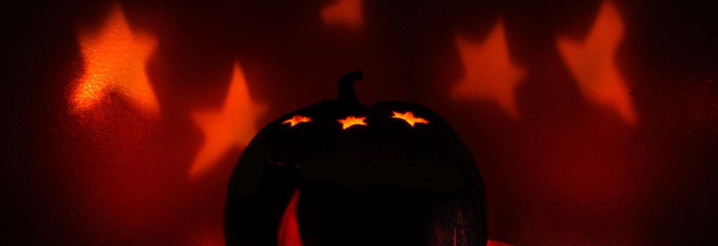 A pumpkin is carved with a crescent moon on the front and stars projecting light on the wall on the back.
