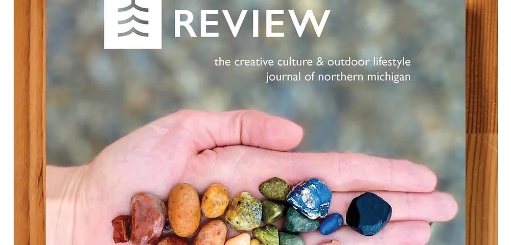 A photo showing the cover of The Boardman Review, which has a hand holding a spectrum of colorful beach stones.