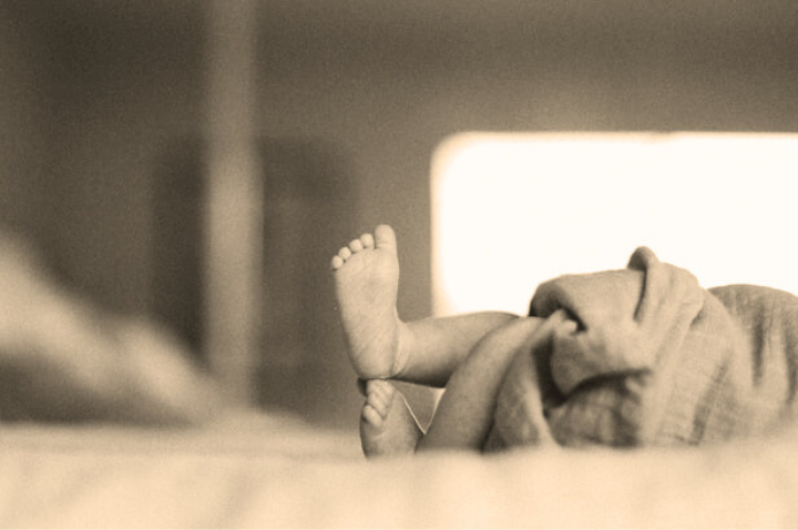 A sepia photograph of a newborn with its two feet stacked on top of the other and a section of blanket
