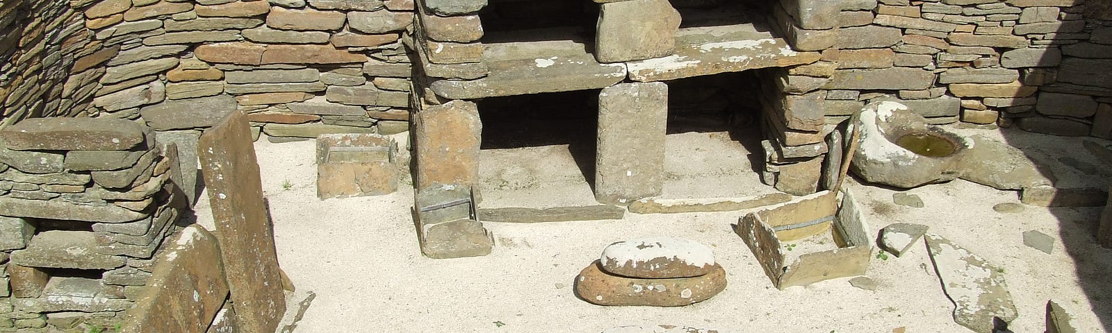 View looking down into a Neolithic house: hearth bottom centre, beyond quern stones, bond shelving; left part of a box bed with double shelving recesses.
