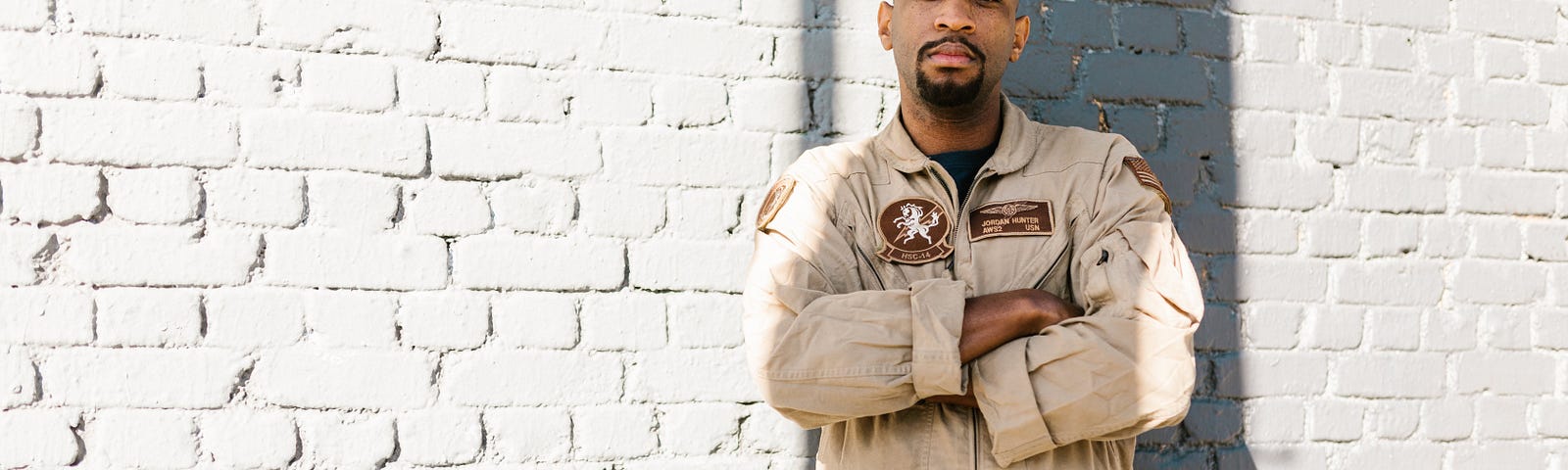 An African-American Veteran standing in front of a brick wall with arms crossed.