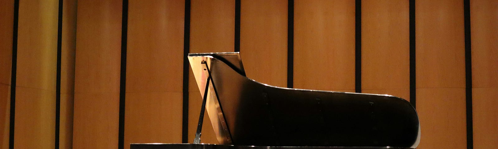A solitary grand piano and a stool stand on the stage of a concert hall.