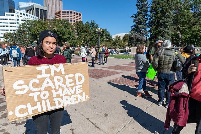 A young woman at a protest rally holds a sign saying, “I’m scared to have children.”