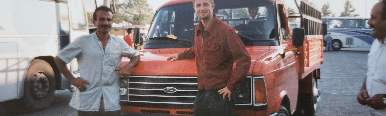 Turkish truck driver standing by his red truck with Gentry Bronson in a red jacket