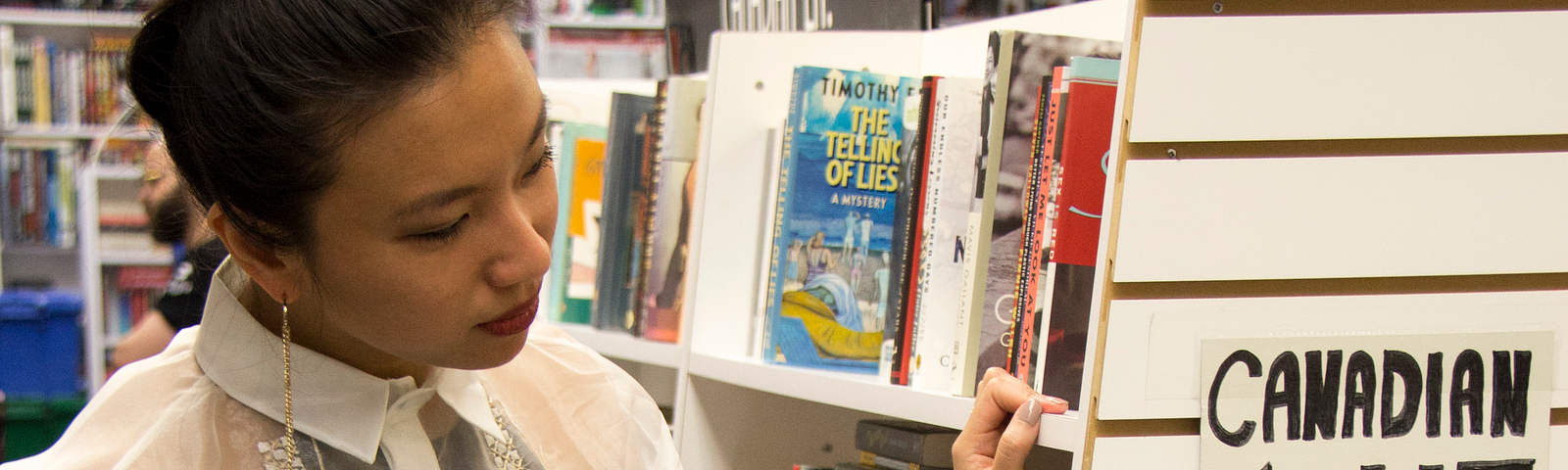 Woman in bookstore aisle looking at a sign that says “Canadian Lit”.