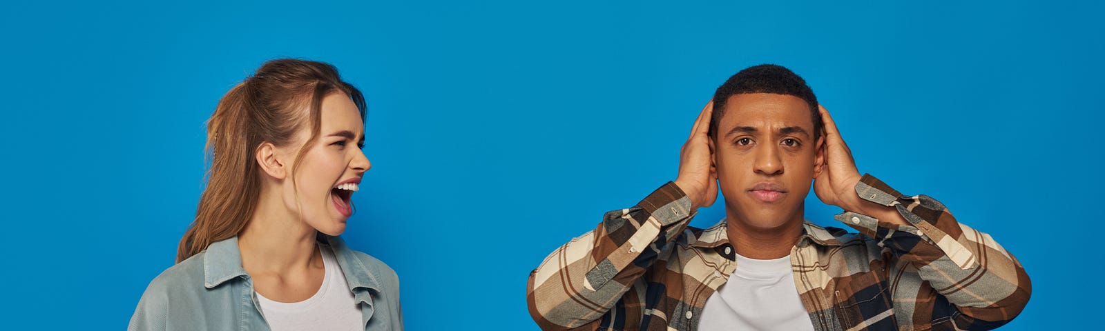 emotional woman screaming near african american man covering his ears on blue background, expressive