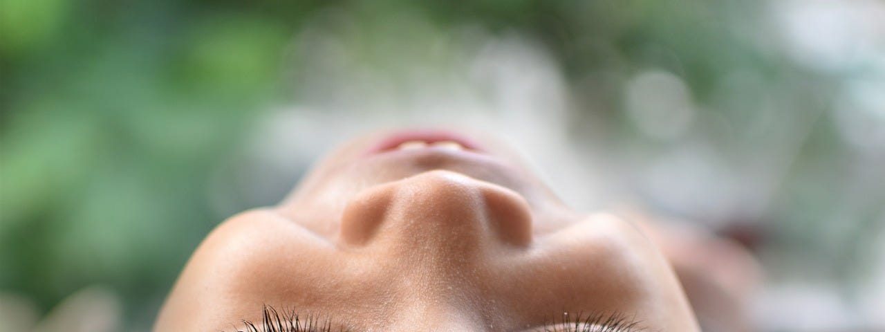 Photo taken from a camera on the ground of a head of a child lying on the grass with eyes closed, smiling