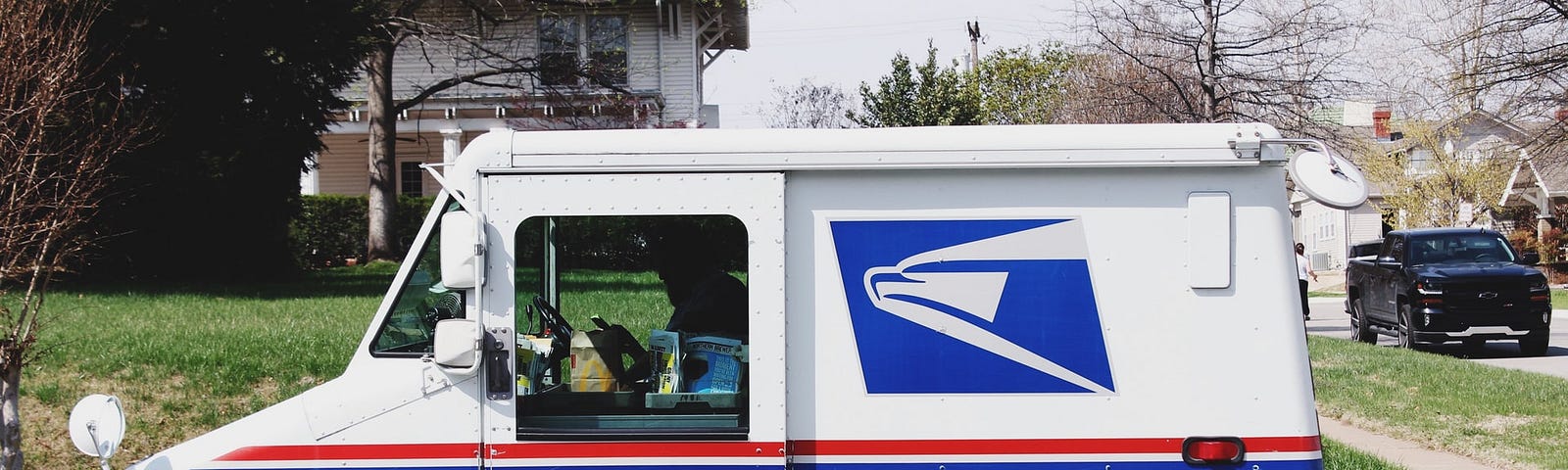 A US Postal Service truck parked on the curb in a residential neighborhood.