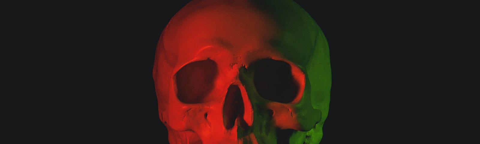 The photo is of a human skull, centered on a black background. It’s cast in read, orange and yellow mood lighting.