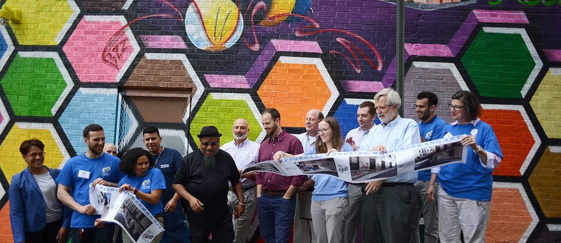 A diverse group of people at a ribbon-cutting for a colorful mural