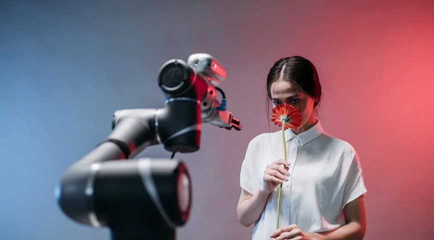 Woman smelling a red flower while staring at a robot arm