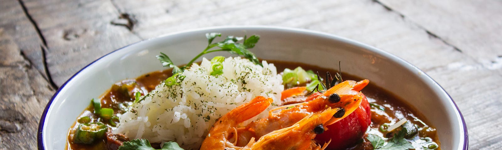 A bowl of gumbo with rice, with multiple shrimp still with the heads on.